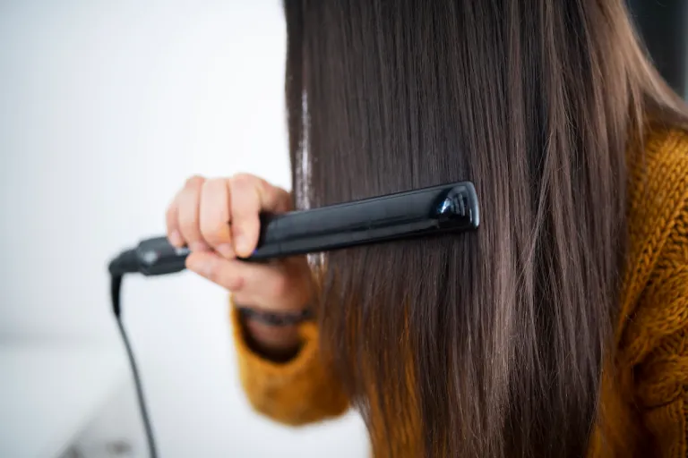 close up brunette woman using hair straightener | MercerOnline